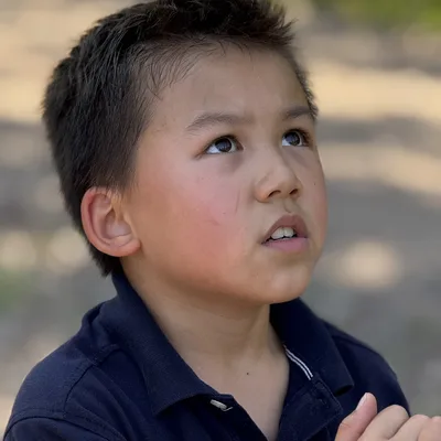A close-up portrait shows a young boy in a dark polo shirt looking upward with a focused expression while holding a white rope. The background is a softly blurred outdoor setting with natural light.